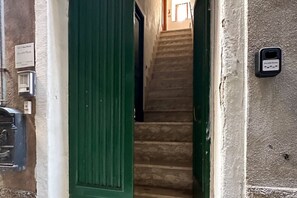 Una escalera que lleva a un piso superior, una puerta verde y un enchufe en la pared.