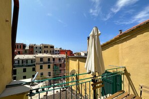 Un balcón con barandilla verde, una sombrilla blanca y vistas de edificios coloridos.