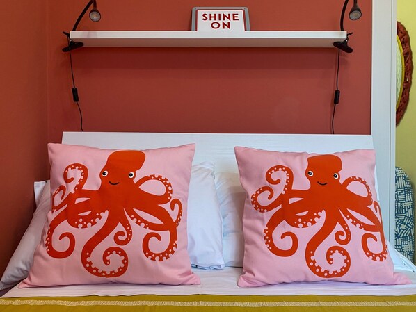 A bed with two pillows featuring an octopus design, a white headboard, and a sign above the headboard that reads 'SHINE ON'.