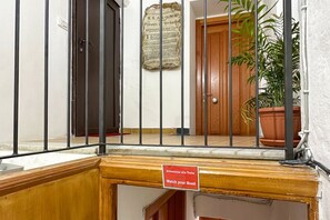 A hotel entrance with a wooden door, a metal gate, a sign reading 'Watch your Head,' and a potted plant.