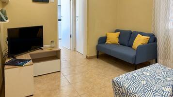 A living room with a TV, sofa, and patterned ottoman.