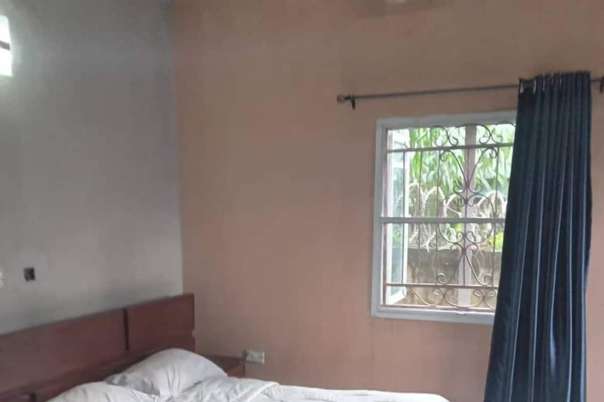 A bedroom with a bed, a window with curtains, and a ceiling fan.