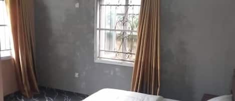 Una habitación con cama, ventana con cortinas, ventilador de techo y piso con diseño de mármol.