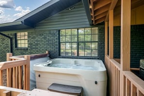 Un jacuzzi en un espacio exterior cubierto con barandas de madera y pared de ladrillo.