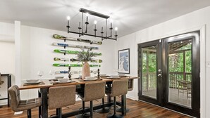 A dining area with a wooden table, four chairs, a vase with flowers, and skis mounted on the wall.