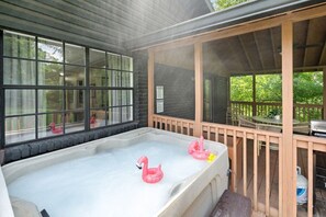 A hot tub with pink flamingo floats, a wooden deck, and a view of greenery.