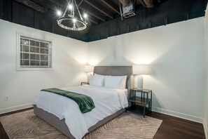 Ein Schlafzimmer mit einem Bett, Nachttischlampen, einem Fenster mit Jalousien und einer Chandelier.