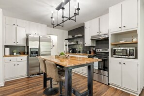 A modern kitchen with white cabinetry, a wooden island, stainless steel appliances, and a black chandelier. - Crestwood Lodge: Hot Tub & Pets! (Birmingham)
