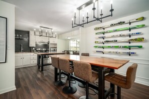 Eine moderne Küche mit weißen Schränken, einer zentralen Kochinsel und einem Essbereich mit Holztisch und Barhocker.