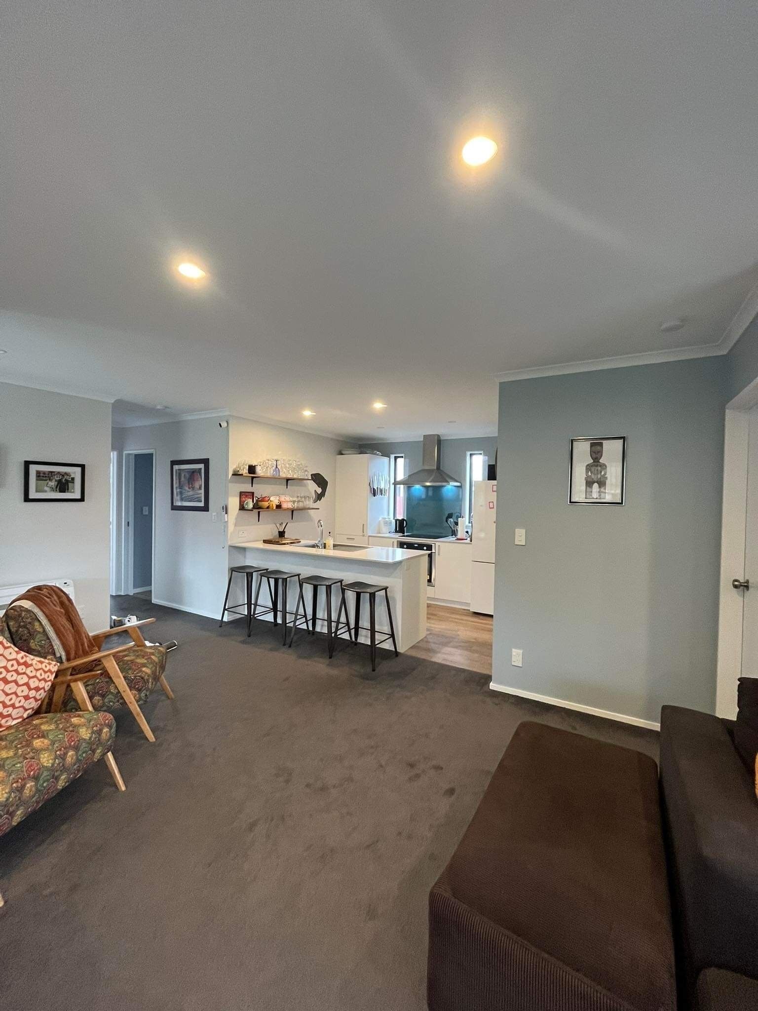 A modern living room with a large sofa and a coffee table, a kitchen area with a central island and bar stools, and a dining area with a table and chairs.