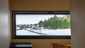 Een kamer met een groot raam dat uitkijkt op een besneeerd landschap met huizen en bomen.
