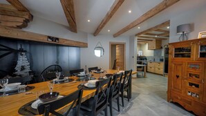 Een eethoek met een houten tafel gedekt voor zes personen, omringd door stoelen, en een keuken op de achtergrond.