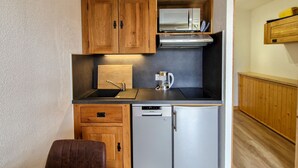 A compact kitchen with wooden cabinets, a stainless steel microwave, a coffee maker, and a dishwasher. - Renovated studio with cabin in Flaine, sunny balcony (Flaine)