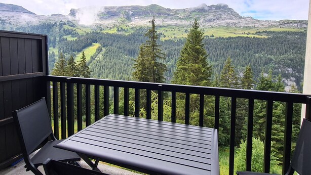 A balcony with a table and chairs, overlooking a mountainous landscape with dense forests and a river. - Renovated studio with cabin in Flaine, sunny balcony (Flaine)