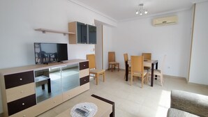 Un salon moderne avec un téléviseur à écran plat, une table à manger en bois avec des chaises, un canapé et un meuble sur lequel est posé un téléviseur.