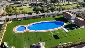 Une vue aérienne d’une piscine entourée d’une pelouse verdoyante, d’un terrain de basketball et d’un petit bâtiment.