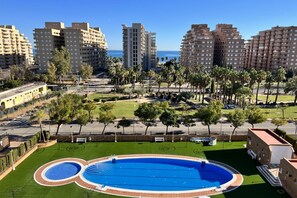 A residential area with a large circular swimming pool surrounded by green lawns and palm trees.