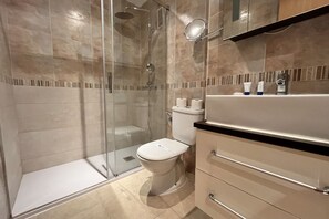 A modern bathroom with a glass-enclosed shower, a toilet, and a vanity with drawers and a mirror.