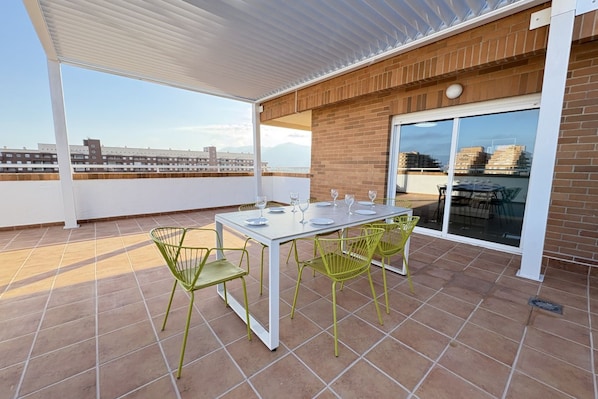 A covered outdoor patio with a table and chairs, a view of the cityscape, and a brick wall.