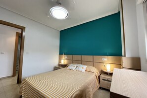 A bedroom with a bed, bedside tables, a nightstand, a ceiling light, and a teal accent wall.