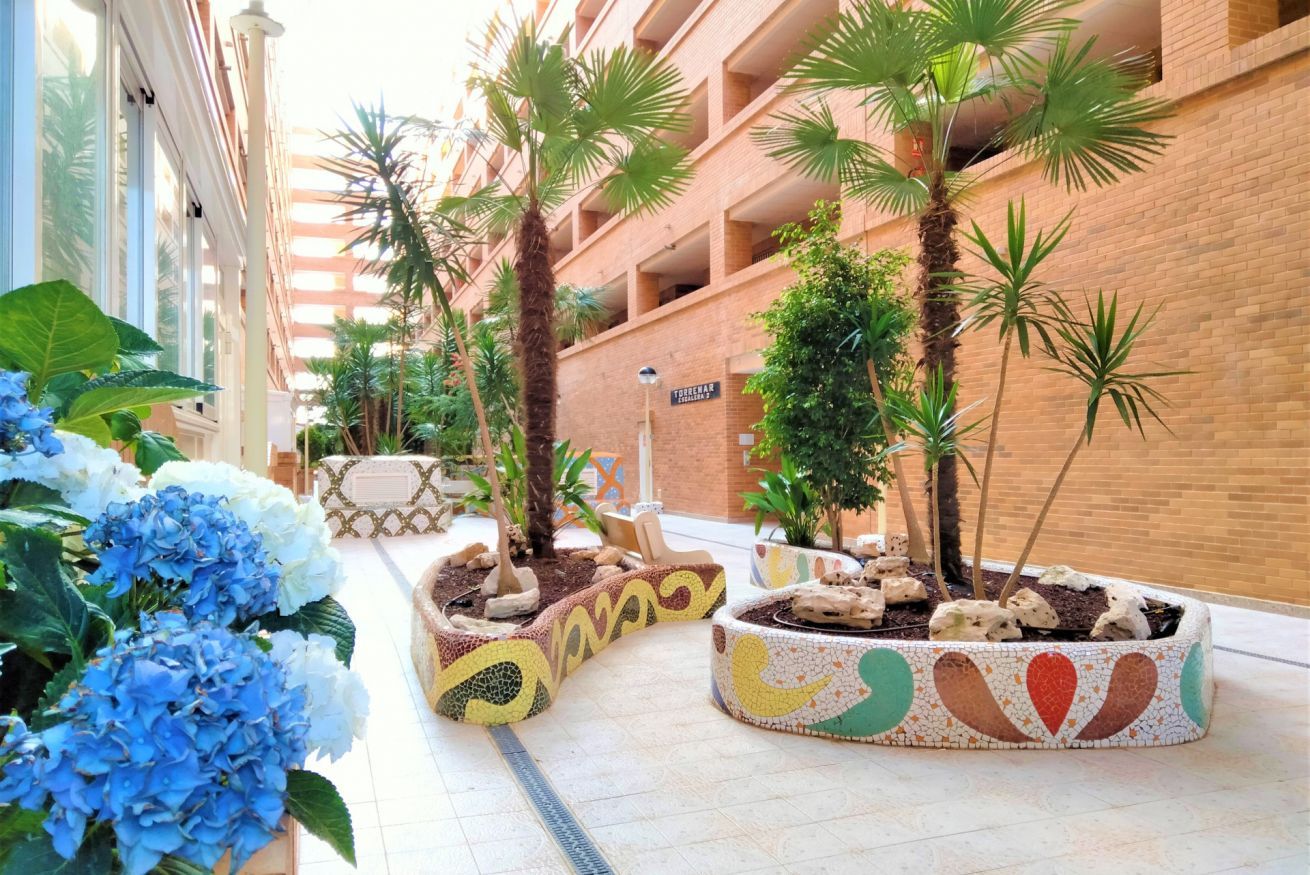 Un couloir d’hôtel avec un sol carrelé, des plantes en pot et un panneau indiquant le nom de l’hôtel.