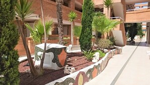 A courtyard with a tiled mosaic border, palm trees, and a brick building with balconies. - ACV - Torremar-2nd line 7th floor Frontal (Oropesa)