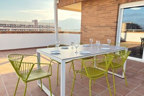 A terrace with a white table and green chairs, overlooking a cityscape.