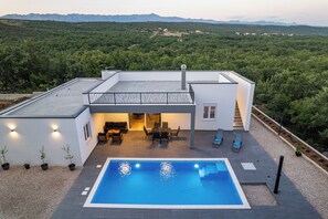 Une maison moderne dotée d’une piscine, d’un espace salon extérieur et offrant une vue sur la forêt environnante.