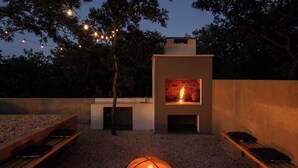 Patio esterno con camino integrato, panche e luci decorative a tenda.