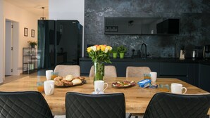 Zona pranzo moderna con tavolo in legno, sedie imbottite nere, un vaso di fiori e prodotti per la colazione.