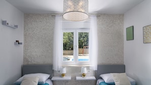 Camera da letto con due letti, una finestra con tende, un lampadario e vista su una piscina esterna.