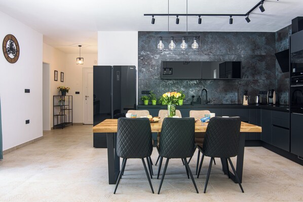 Une cuisine moderne avec des meubles de rangement noirs, une table à manger en bois et des chaises noires.