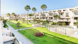 A residential complex with multiple apartment buildings, a well-maintained lawn, and palm trees.