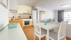 A modern kitchen with white cabinets, a built-in oven, and a dining area with a white table and chairs.