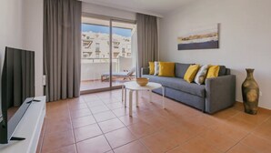 A modern living room with a grey sofa, yellow cushions, a white coffee table, and a large window with a view of buildings.