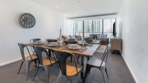 Un espace repas moderne avec une table en bois dressée pour quatre personnes, des chaises noires et une grande horloge murale.