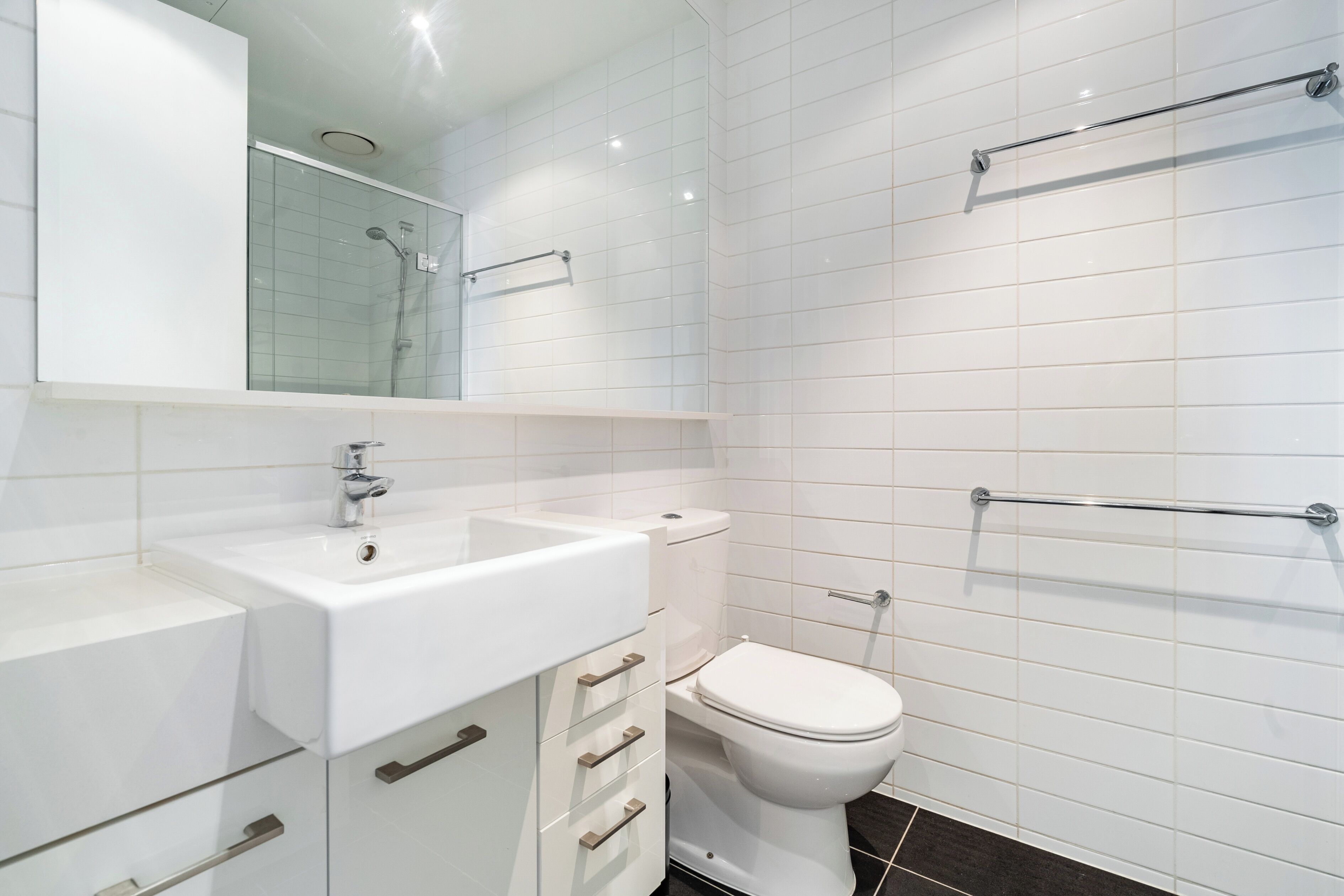 A modern bathroom with a white sink, mirror, and toilet.