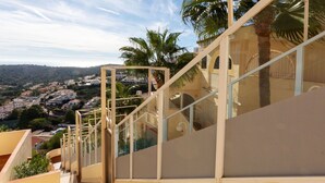 A staircase leading to a balcony with glass railings, overlooking a residential area with palm trees and houses.