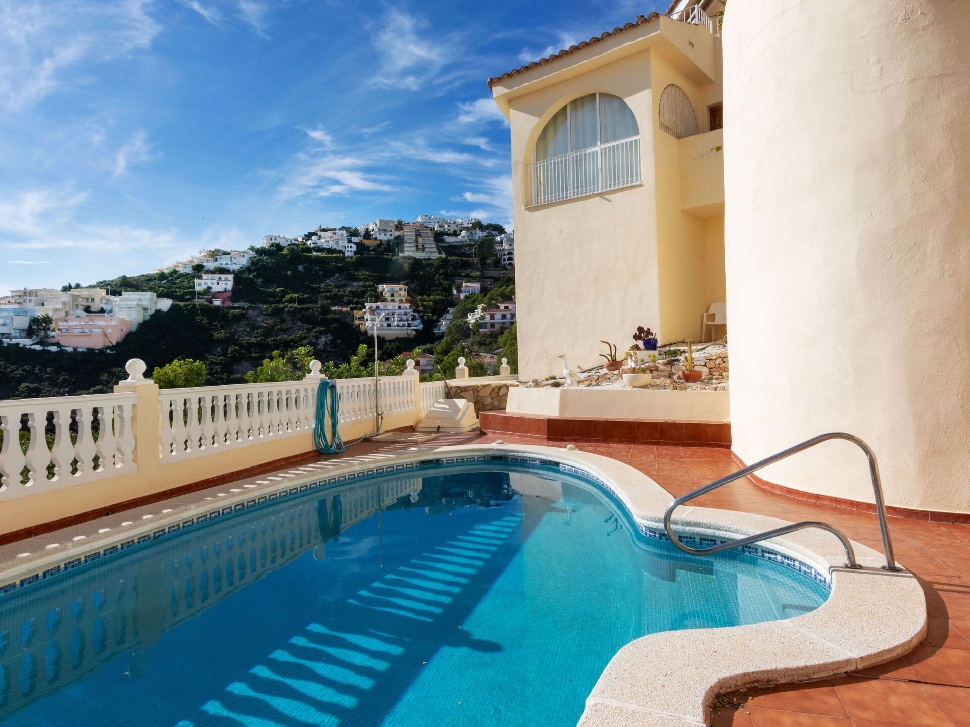 Ein Swimmingpool mit Blick auf einen Hügel mit weißen Gebäuden unter blauem Himmel.