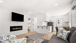 A modern living room with a flat-screen TV, a fireplace, a sofa, and a dining area. - Nicely Updated Two Bedroom Midtown Oceanside Condo (Ocean City)