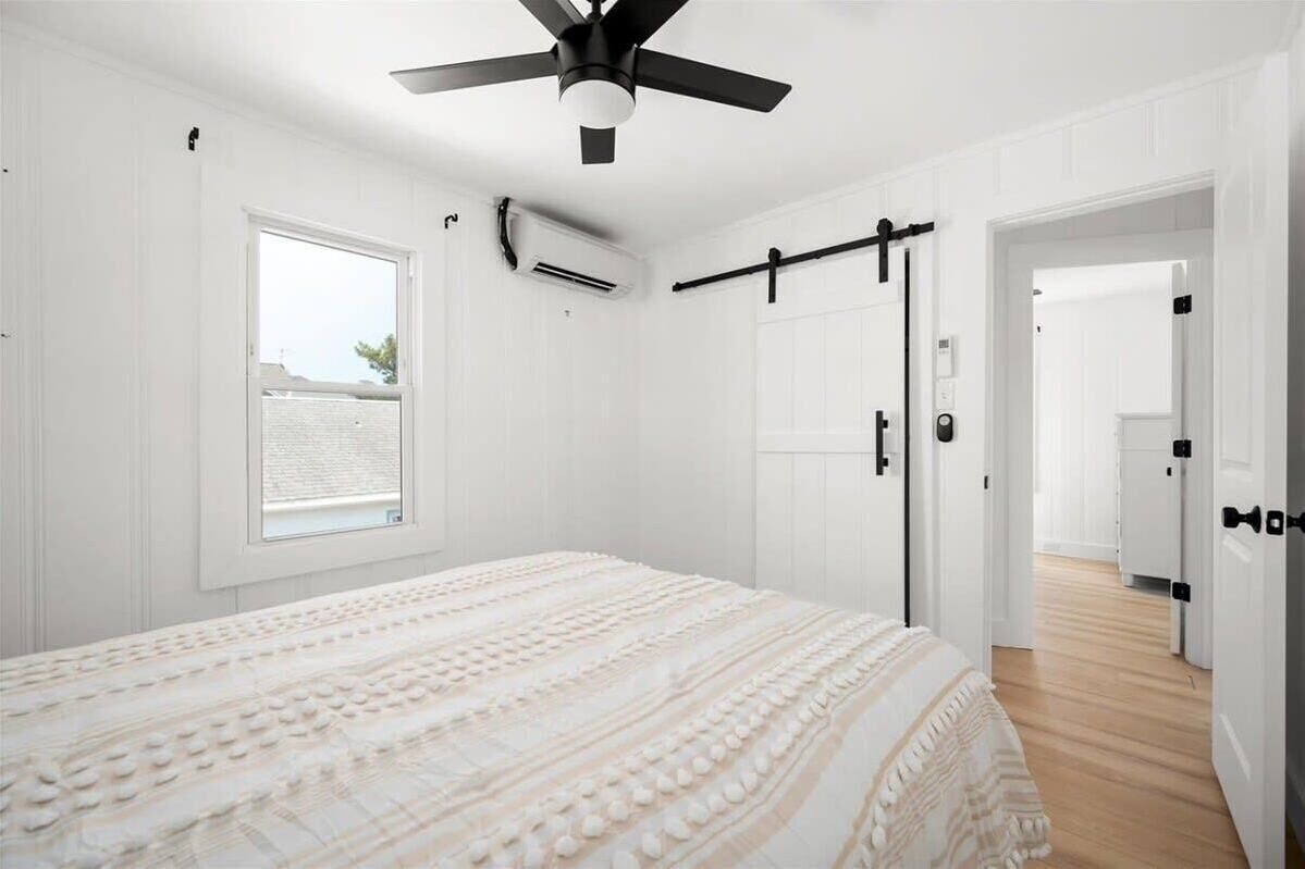 Ein Schlafzimmer mit einem Bett, einem Deckenventilator, einem Fenster und einer Tür zu einem anderen Raum.