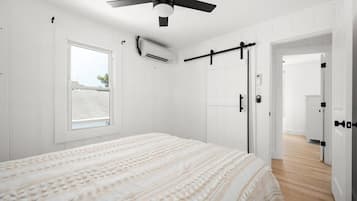 Ein Schlafzimmer mit einem Bett, einem Deckenventilator, einem Fenster und einer Tür zu einem anderen Raum.