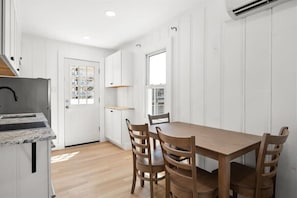 A modern kitchen with white cabinetry, a wooden dining table, and chairs. - Nicely Updated Two Bedroom Midtown Oceanside Condo (Ocean City)