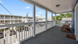 A covered porch with white railings, a view of a parking lot, and a building in the background. - Nicely Updated Two Bedroom Midtown Oceanside Condo (Ocean City)