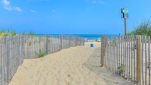 A sandy beach path leading to the ocean with a wooden fence on one side and a signpost on the other. - Nicely Updated Two Bedroom Midtown Oceanside Condo (Ocean City)
