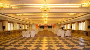 Un salón de banquetes con piso a cuadros, hileras de sillas blancas y un escenario central.