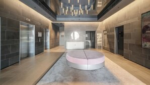 A modern lobby with a central seating area, elevators, and a large circular light fixture. - Mega Style Apartments Bella (Southbank)