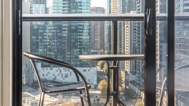 A balcony with a chair and table, overlooking a cityscape with tall buildings. - Mega Style Apartments Bella (Southbank)