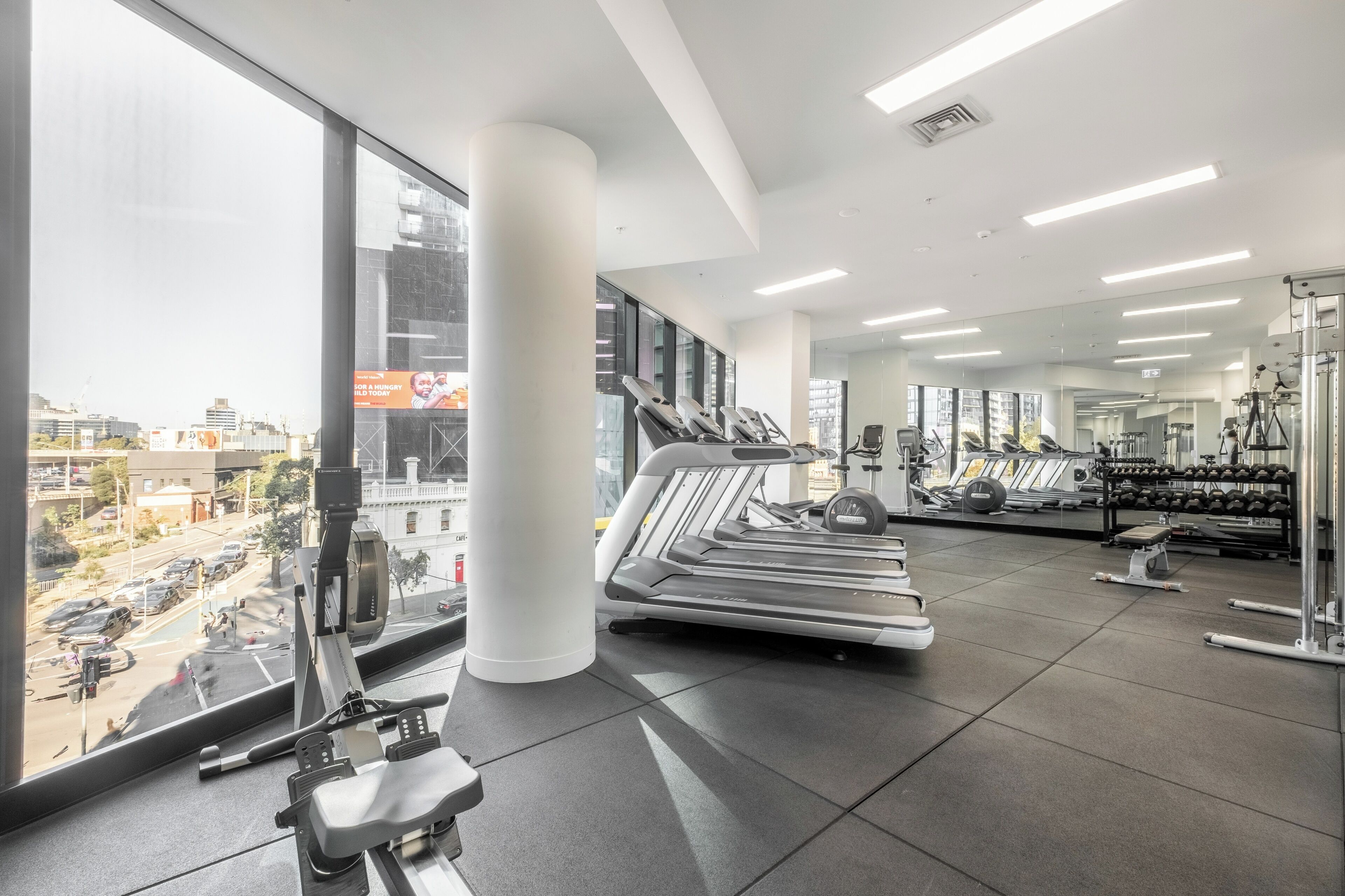 Un gimnasio moderno con equipamiento de cardio, máquinas de pesas y grandes ventanales con vistas a la ciudad.