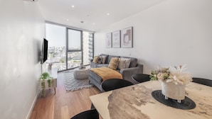 A modern living room with a grey sofa, a coffee table, and a TV mounted on the wall. - Mega Style Apartments Bella (Southbank)